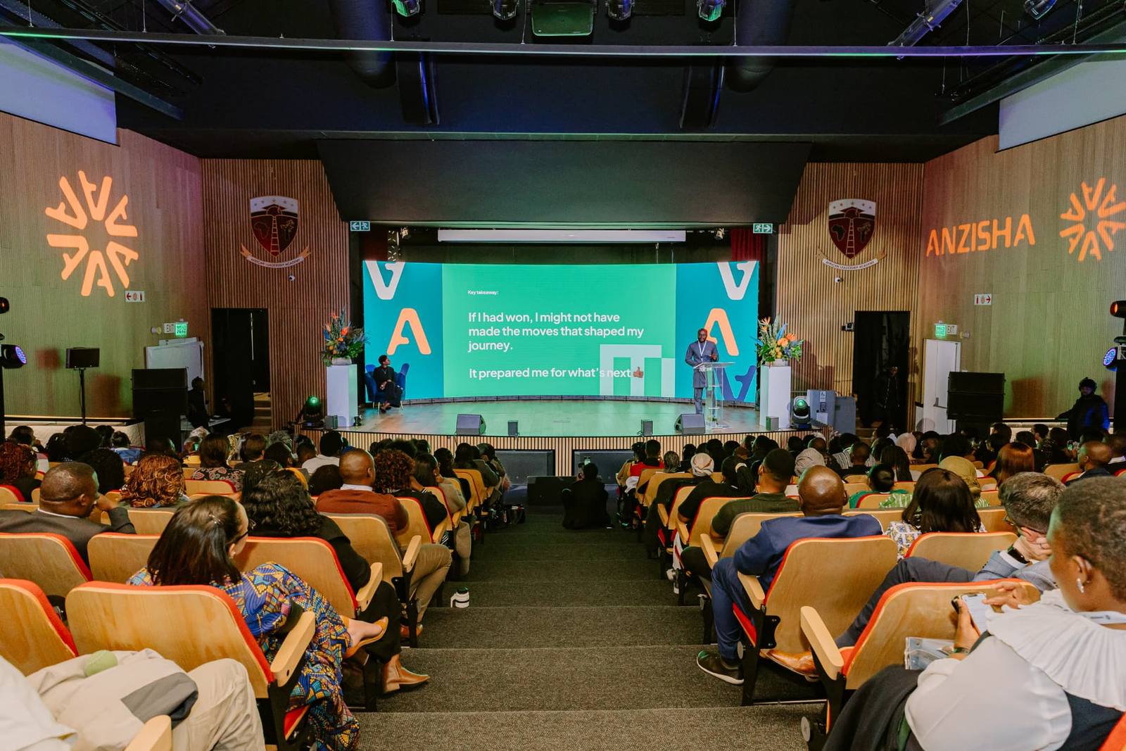 Keynote speaker on a lit auditorium stage with LED backdrop